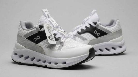 Tenis blancos para mujer con paneles en gris y negro, par completo sobre fondo gris